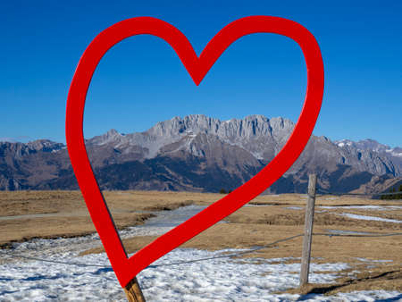 Amazing landscape to the Presolana mountain range through a red wooden heart. View in winter dry season. Landscape from Monte Pora. Orobie alps, Bergamo, Lombardy, Italyの写真素材