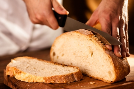 Baker Slicing Bran Bread on a Cutting Boardの写真素材