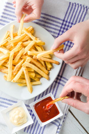 Three Hands Picking French Fries and Dipping in Ketchup and Mayonnaiseの写真素材