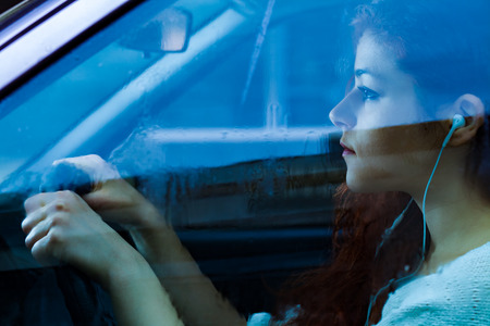 Woman with Earbuds Driving a Car on a Rainy Day