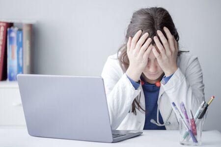 Tired Young Woman Doctor Working with a Laptop in a Clinicの写真素材