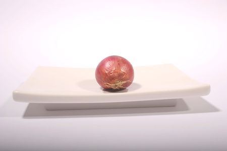 A red unpeeled onion on a white plate against a white backgroundの写真素材