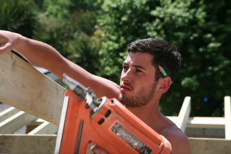 A construction worker uses a nail gun to secure roof timbers