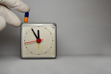  fingers keeping medicine. A clock shows 11:55 a.m or p.m.の写真素材