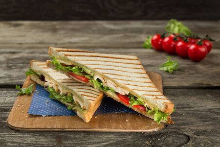 Club sandwich with chicken breast, tomato, cheese and green salad served on the woodenの写真素材