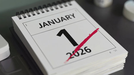 A close-up, realistic shot of a modern, spiral-bound desk calendar showing the date "January 1, 2026" boldly printed, with a striking red line crossing it out. The image symbolizes deadlines, the start of a new year, goal setting, or important dates.の素材