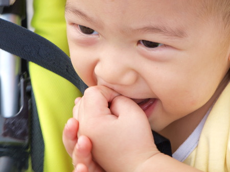 asian baby bite his finger in sitting strollerの写真素材