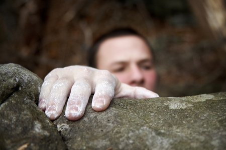 A climber reaches the top of a boulder. His visible hand is covered in white chalk, and his face is just peeking over the edge.の写真素材