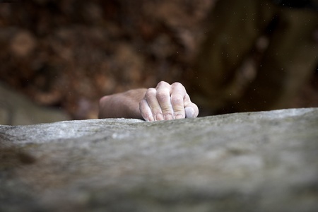 Grabing onto a small handhold, a climber makes his way to the top. His hand is covered in chalk, and...