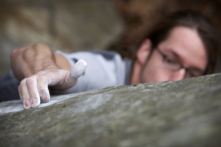 A man grasping onto a boulder in an attempt to reach the top of a hard climb. He is peaking over the...