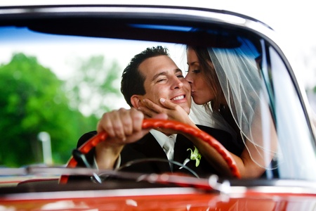 A bride giving her groom a kiss while he sits inside a car and smilesの写真素材