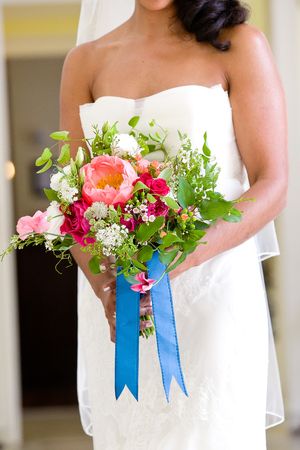 bride holding her wedding bouquet of flowers with blue ribbons and pink and red flowersの写真素材