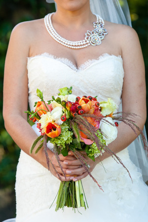 bride holding her wedding bouquet of flowers with green, red, white, and orange flowersの写真素材