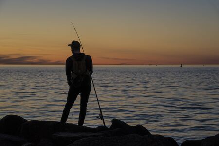 Silhouette of a man fishing at sunsetの写真素材