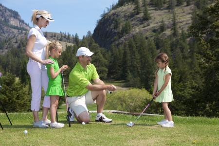 Outdoor photo of young family of four on golf course, father is instructing child.の写真素材