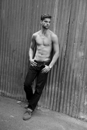 Outdoor photo of handsome, shirtless young man standing against grunge metal wall.の写真素材