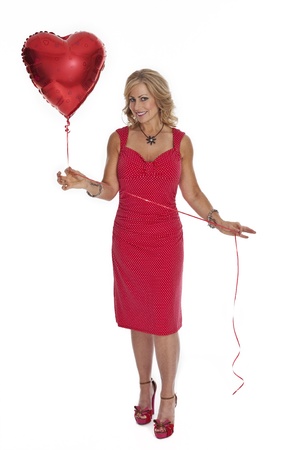 Full length photo of 40 year old woman in red dress holding heart shaped red balloon on white background.の写真素材