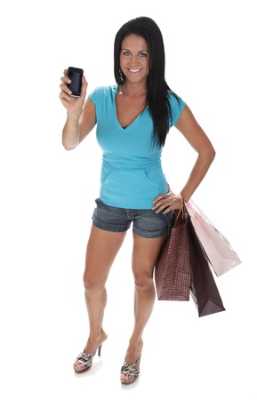 Full length photo of attractive young woman standing on white background holding smart phone and shopping bags.の写真素材
