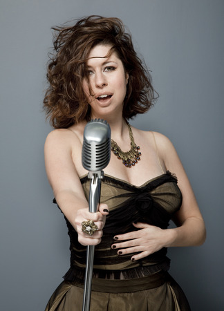 Front view studio photo of attractive young adult singer with microphone on gray background.の写真素材