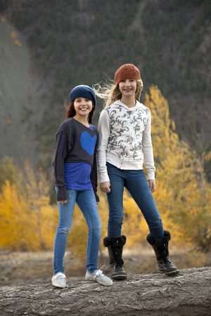 Two Adolescent girls standing on log in outdoor autumn settingの写真素材
