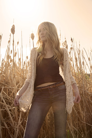Low angle, outdoor photo of pretty young woman standing in dry grass, backlit, low contrast with warm hues.の写真素材