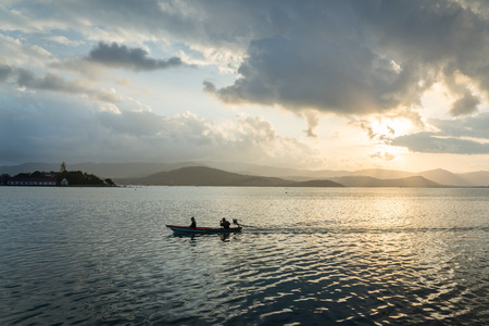 silhouette fisherman in small boat pass through the sea and sundow behind the mountain and phra yai in samui, thailandの写真素材