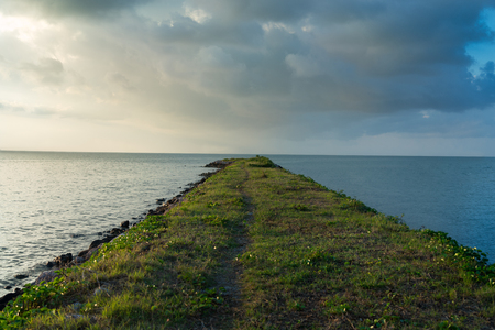 walk on road to the ocean and cloudy sky with sunset in the left sideの写真素材