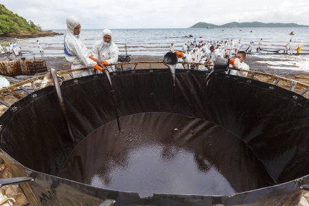 RAYONG, THAILAND - JULY 31, 2013  Workers in biohazard suits pouring spilled crude oil into big tank as cleaning operations from a beach of Samet Island on July 31, 2013 in Rayong, Thailand のeditorial素材