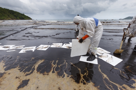 Rayong, Thailand - July 31, 2013  A Worker in biohazard suit placing absorbent paper in a clean-up operation of crude oil spilled at Ao Prao Beach on July 31, 2013 in Koh Samet, Rayong, Thailand のeditorial素材