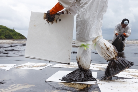 Rayong, Thailand - July 31, 2013  A Worker in biohazard suit placing absorbent paper in a clean-up operation of crude oil spilled at Ao Prao Beach on July 31, 2013 in Koh Samet, Rayong, Thailand のeditorial素材