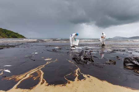 Rayong, Thailand - July 31, 2013  A Worker in biohazard suit placing absorbent paper in a clean-up operation of crude oil spilled at Ao Prao Beach on July 31, 2013 in Koh Samet, Rayong, Thailand のeditorial素材