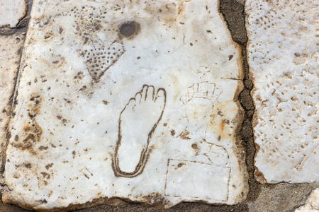 A marble slab pavement engraved with a woman's head, a broken heart, money, and a left foot pointing in the direction of the brothel in Ephesus, the ancient Greek city in Turkey.の写真素材