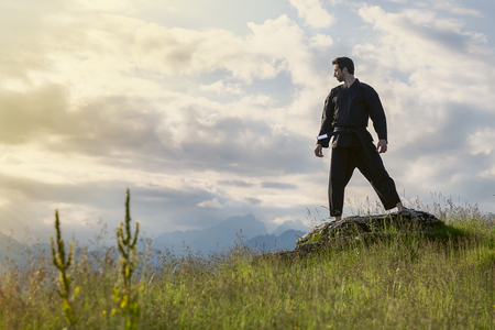 A man in uniform with a black belt trains karate on top of a mountain against the background of the sky and mountains. Performs kata elements.の写真素材