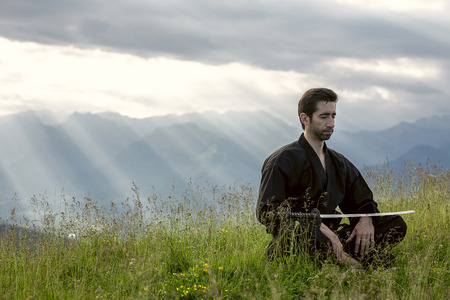Man in kimono meditating on the grass in the mountainの写真素材
