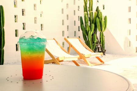 Cool rainbow soda on a chair background and blurred cactus.