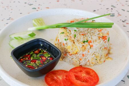 Crab fried rice topped with tomatoes and spring onions on a white plateの写真素材