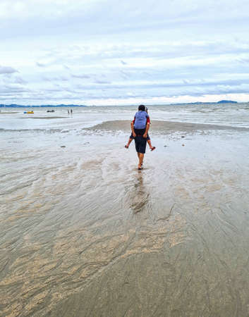 The son rides on his father's back and walks by the sea.の写真素材