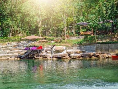 A seat by the waterfall surrounded by bright green nature.の写真素材