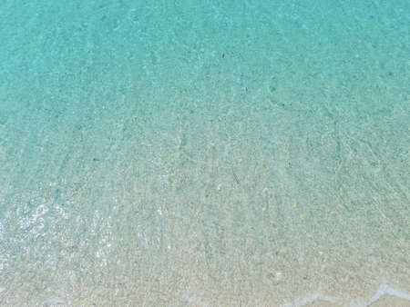 Light blue sea waves on a sandy beach background.