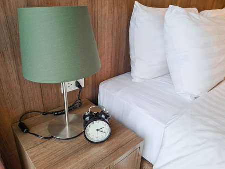 A room with a table lamp and a clock next to the bed.