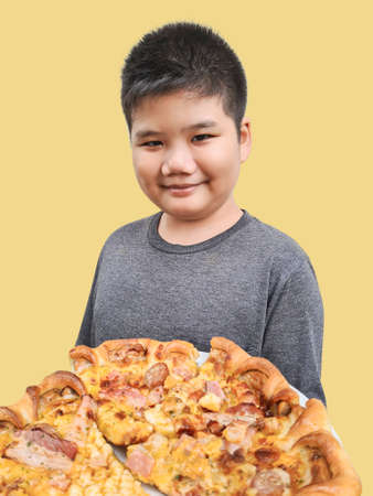 boy holding pizza Close-up of smiling child with delicious pizza, isolated on yellow background. Children show fast foodの写真素材