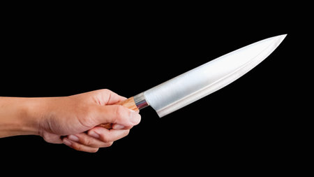 Male hand holding knife on isolated black background.