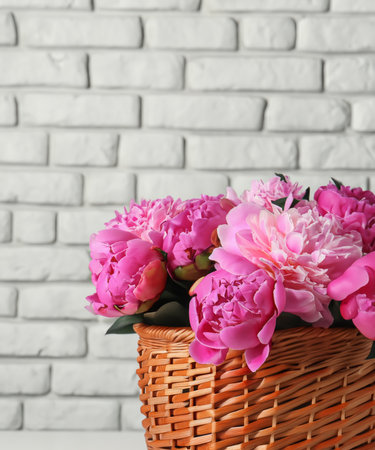 Beautiful peonies in wicker basket on white table near brick wallの素材