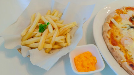 Delicious french fries, cheese sauce and pizza on the table.