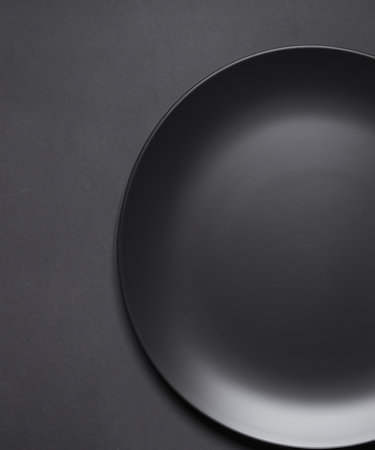 Empty round black plate on dark moody black  background with copy space. Overhead viewの素材