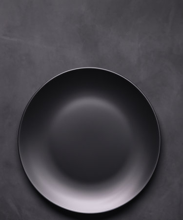 Empty round black plate on dark moody black  background with copy space. Overhead viewの素材