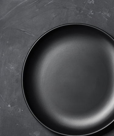 Empty round black plate on dark moody black  background with copy space. Overhead viewの素材
