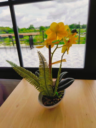 Yellow fake flowers on the wooden table by the windowの写真素材