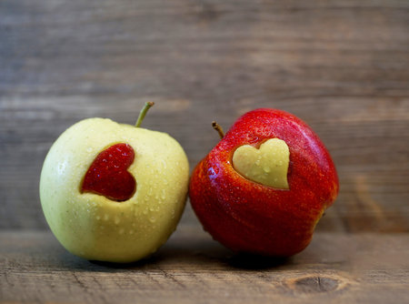 Two red and yellow apples with heart shaped holes on wooden background.の素材