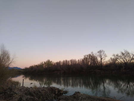 Sunset on the river with trees in the foreground and a blue sky